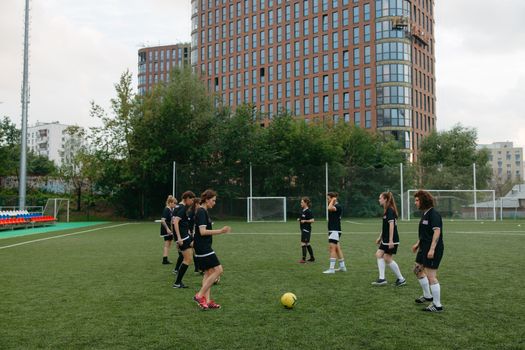 Energetic women's soccer team practicing on a green field with urban buildings in the background.