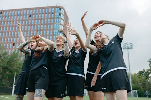 A joyful moment with women soccer players celebrating victory on an outdoor field with a building backdrop.