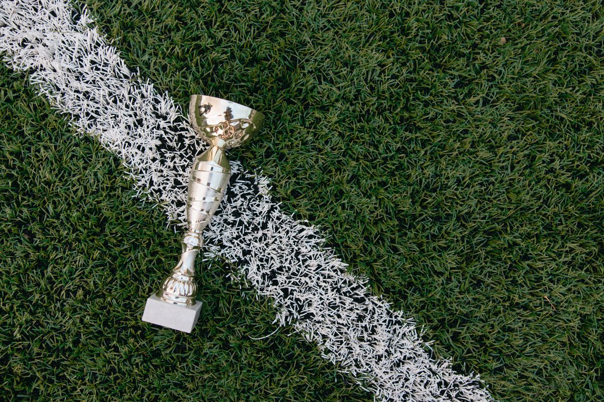 Yeşil çim üzerinde futbol topu ve altın renkli kupa ödülü
