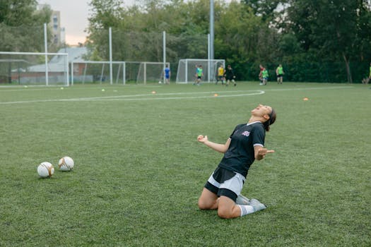 Female soccer player celebrating with arms raised on outdoor field.