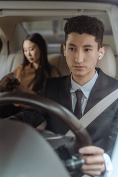 Professional driver in black suit focused on the road with a passenger in the backseat.