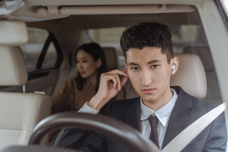 A Man In Black Suit Driving A Car