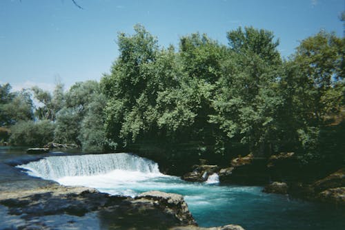 A Waterfalls Near the Green Trees Under the Blue Sky