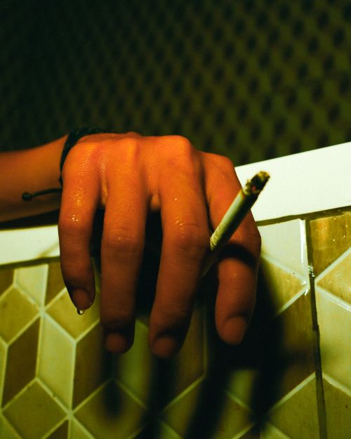 Free Dramatic close-up of a hand holding a cigarette with a wet surface in low light. Stock Photo