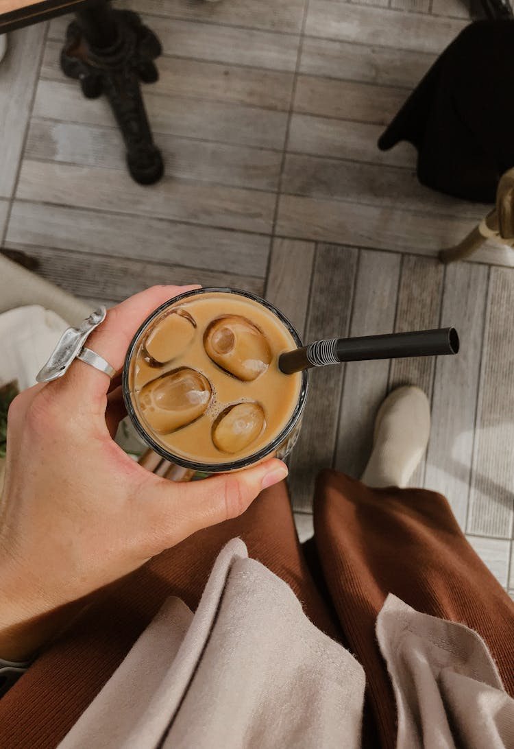 A Person Holding A Glass Of Iced Coffee With Black Straw