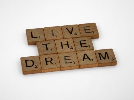 Scrabble tiles spelling 'Live The Dream' on a white surface, conveying motivation.