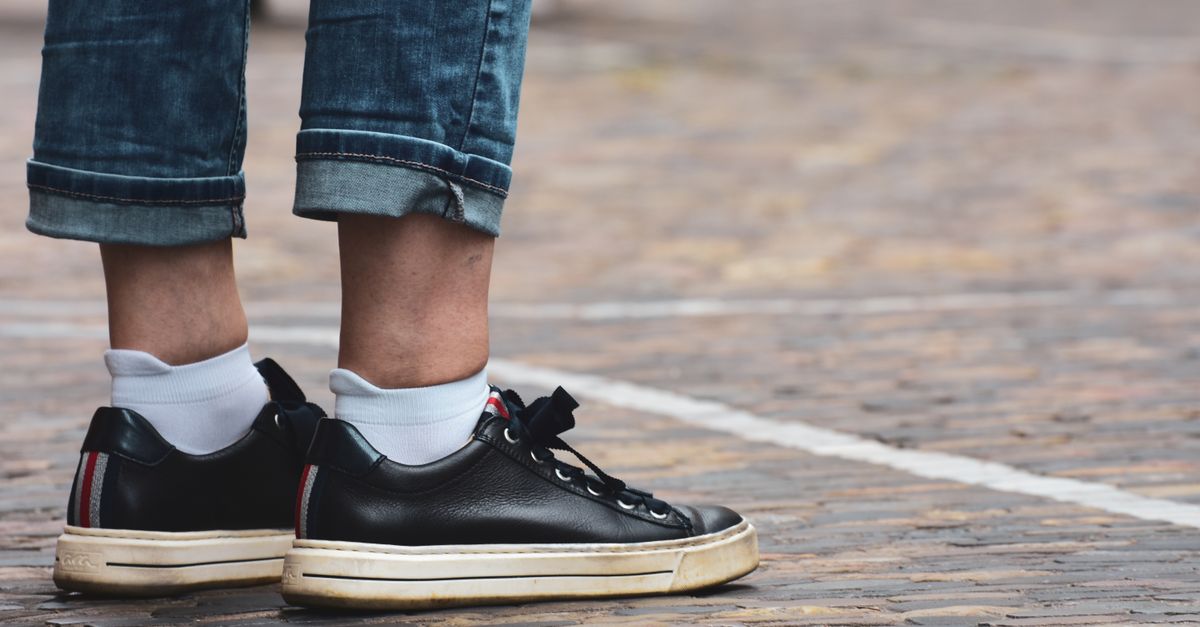 Close-up of a person's legs wearing stylish black sneakers with rolled-up blue jeans outdoors.