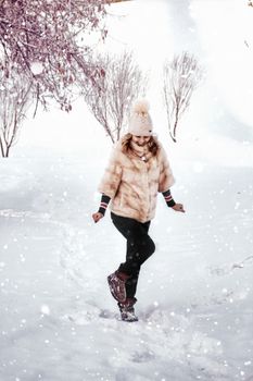 Woman smiling while walking in a snowy landscape, wearing a fur coat and beanie.