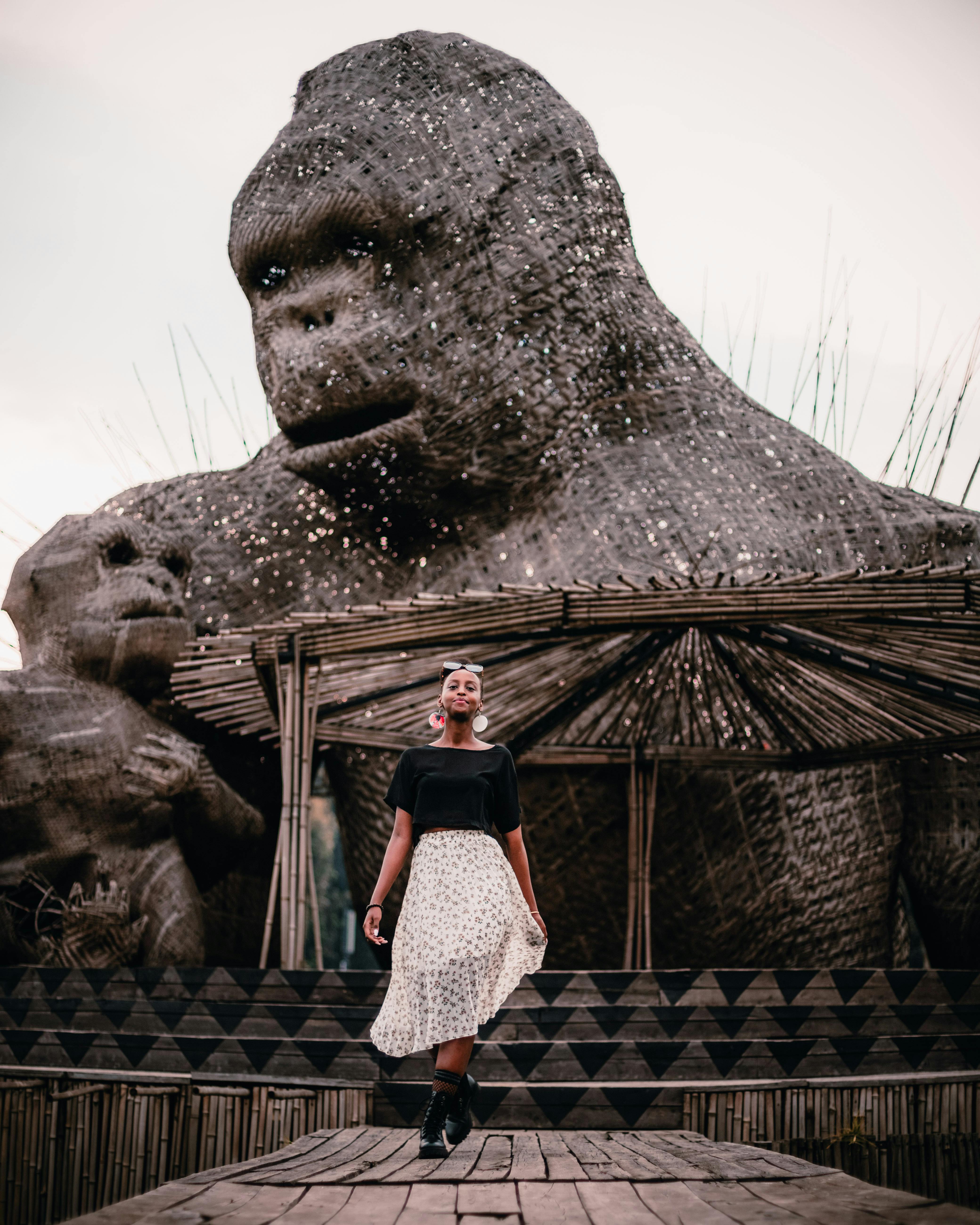 Stylish woman standing in front of monumental ape statue with artistic backdrop.
