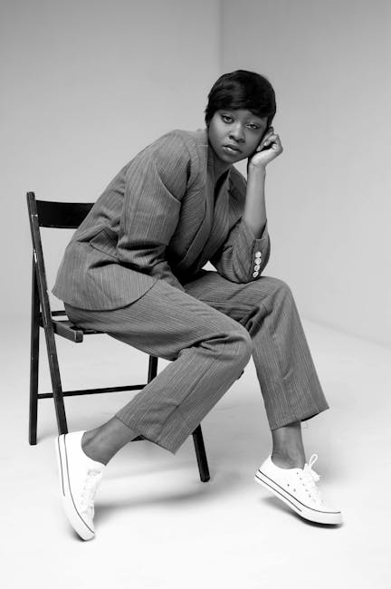 Black and white studio portrait of a fashion model in a suit and sneakers, exuding modern style.