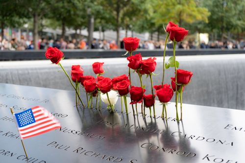 Free Red roses and American flag at 9/11 Memorial in New York City, reflecting remembrance. Stock Photo