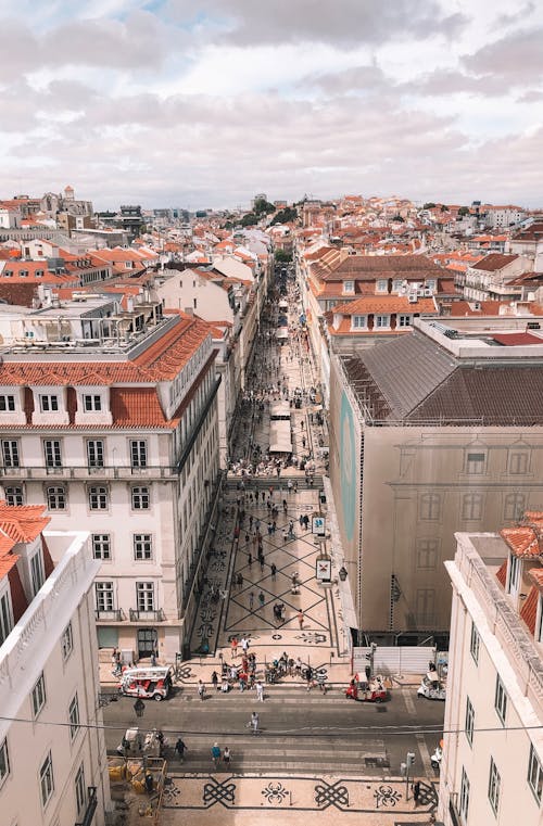 An Aerial View of People Walking on the Street Between City Buildings