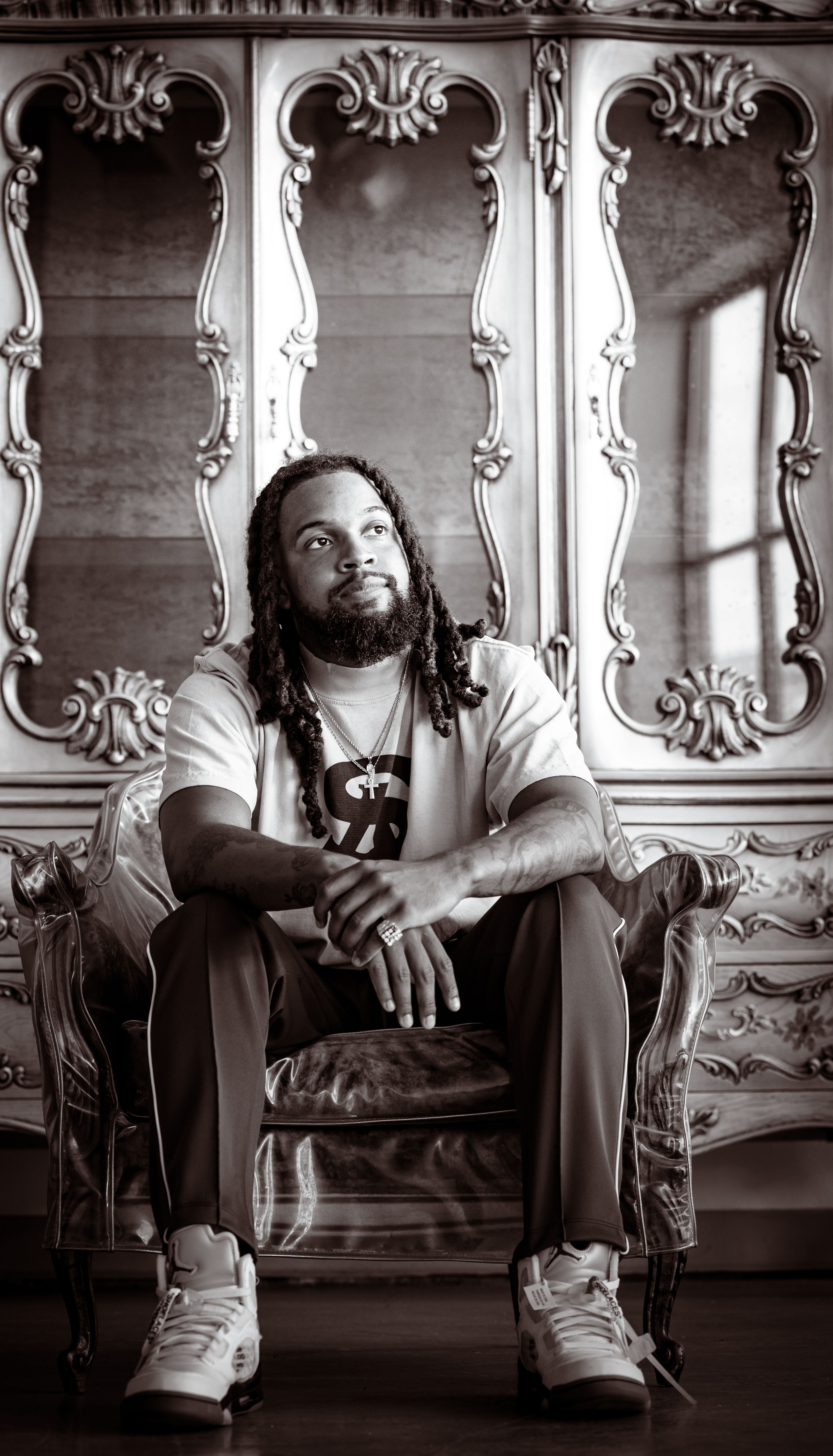 Monochrome portrait of a man sitting in a vintage armchair with ornate background.