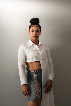 Portrait of a fashionable woman in a denim skirt and white shirt with a neutral background.