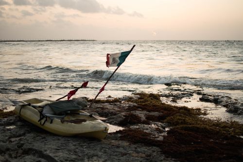 Free Sandy shore of Playa del Carmen with a boat and Mexican flag at twilight on the sea edge. Stock Photo