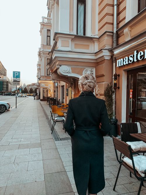 Free Stylish woman in trench coat walking along a city sidewalk lined with shops during daytime. Stock Photo