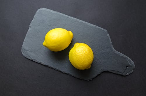 Two Lemons on Black Wooden Pad