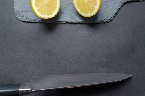 Free Close-up of fresh lemon slices on slate board with a stainless steel chef's knife. Stock Photo