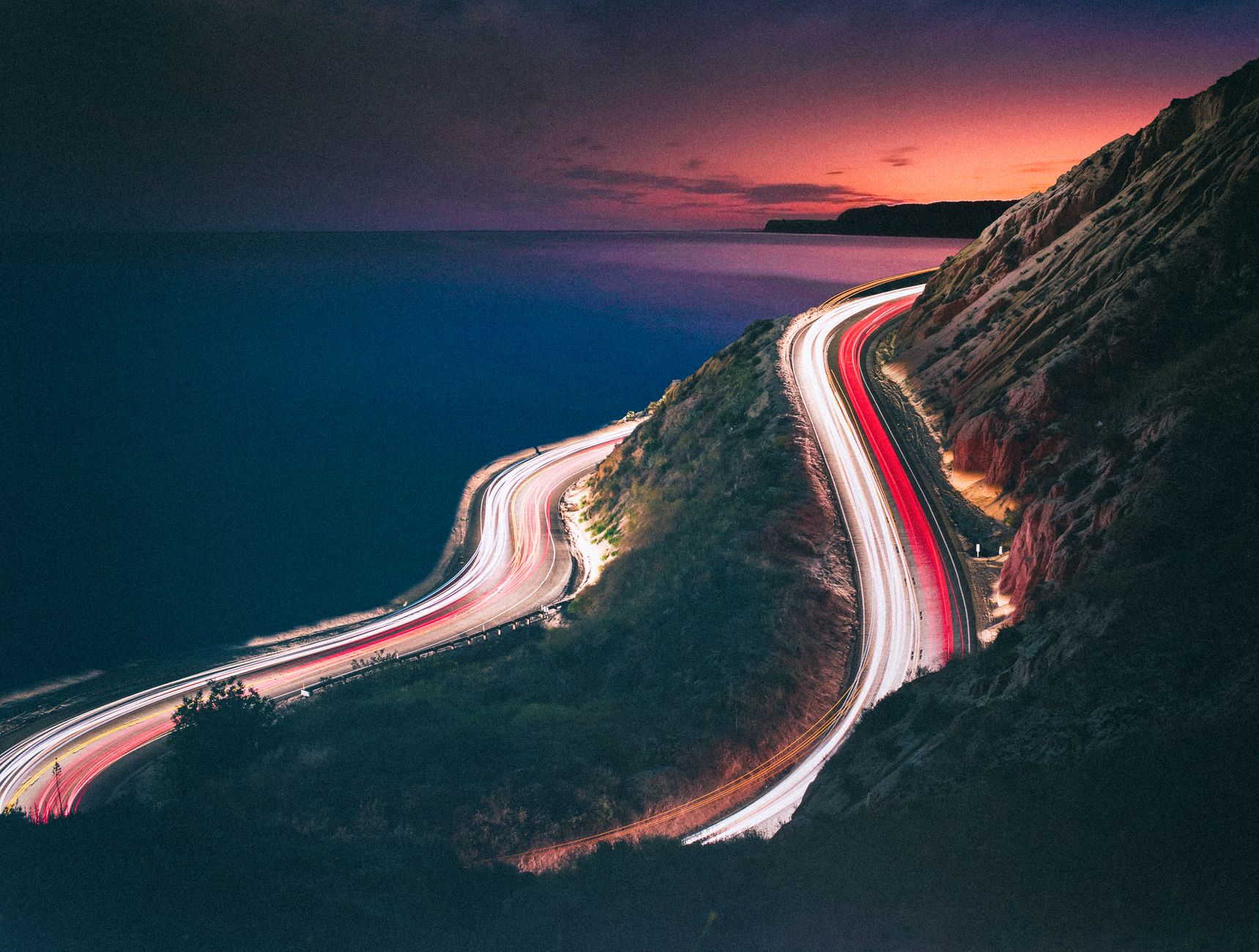 Luxury vehicle driving along the Pacific Coast Highway in Malibu at sunset