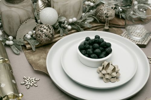 Free Festive holiday dining table set with blueberries, ornaments, and candles in white and gold. Stock Photo