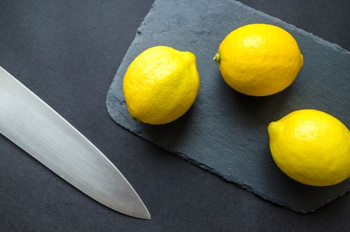 Free Top view of three fresh lemons on a slate board with a kitchen knife, highlighting vibrant citrus theme. Stock Photo