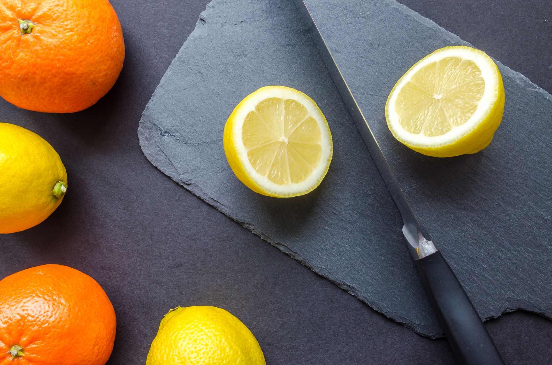 Close-up of sliced lemon with oranges and knife on slate board. Perfect for healthy food themes.