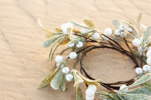 Free Close-up of a decorative mistletoe wreath with glitter on a sandy background, ideal for holiday themes. Stock Photo