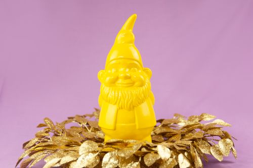 Free Bright yellow garden gnome with a gold leaf decoration against a purple backdrop, perfect for cheerful decor concepts. Stock Photo