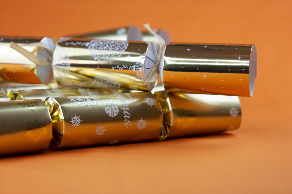 Festive golden Christmas crackers beautifully arranged on a vibrant orange background, perfect for holiday celebrations.