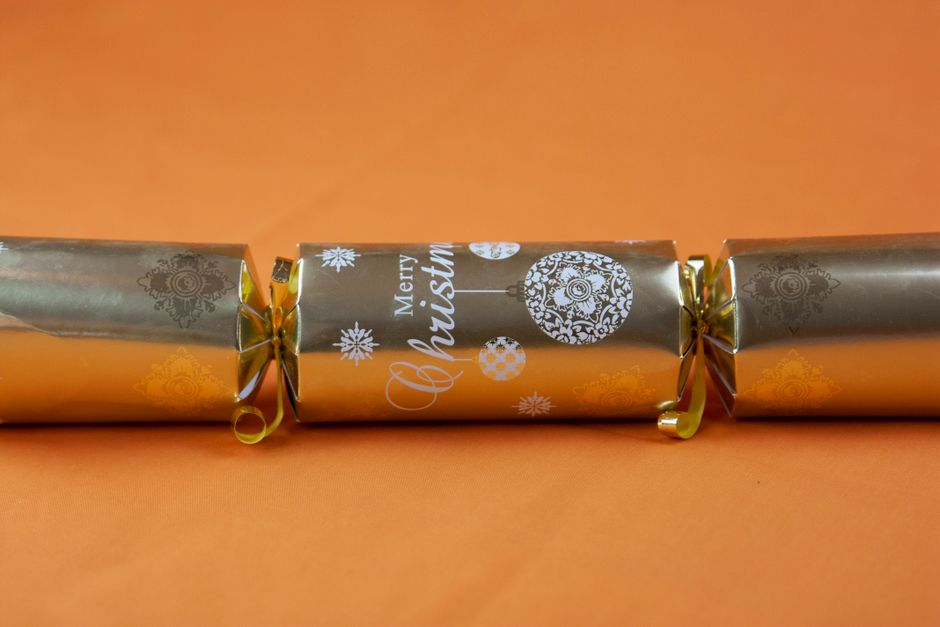 Elegant gold Christmas cracker with festive design on orange backdrop, perfect for holiday celebrations.