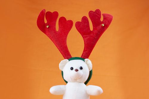 Free Cute white teddy bear wearing red reindeer antlers on an orange background, perfect for Christmas themes. Stock Photo