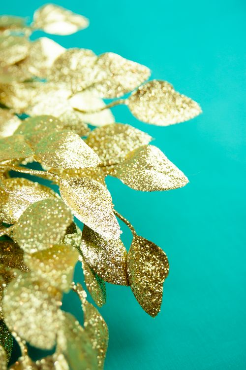Free Close-up of glittery golden leaves against a vibrant turquoise backdrop, ideal for festive decor. Stock Photo