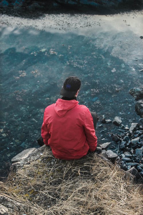 Free Man in Red Hoodie Sitting on Cliff Stock Photo