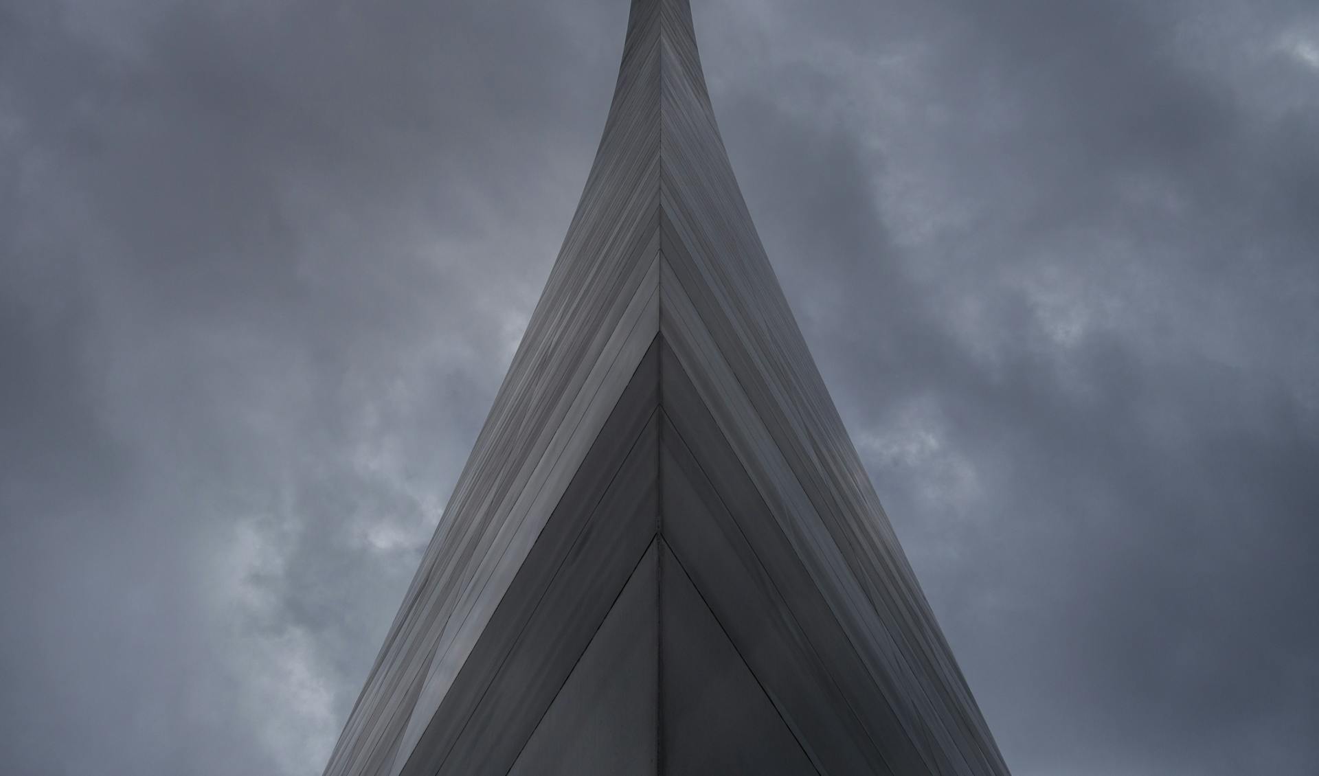 Modern skyscraper with an angular design pierces through a moody cloudy sky.