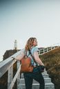 Woman in White Shirt and Brown Backpack Standing on Brown Wooden Bridge