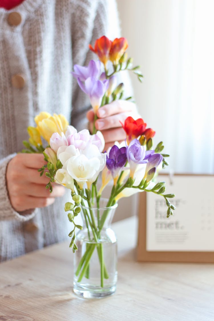 Person Arranging Flowers In A Glass Vase