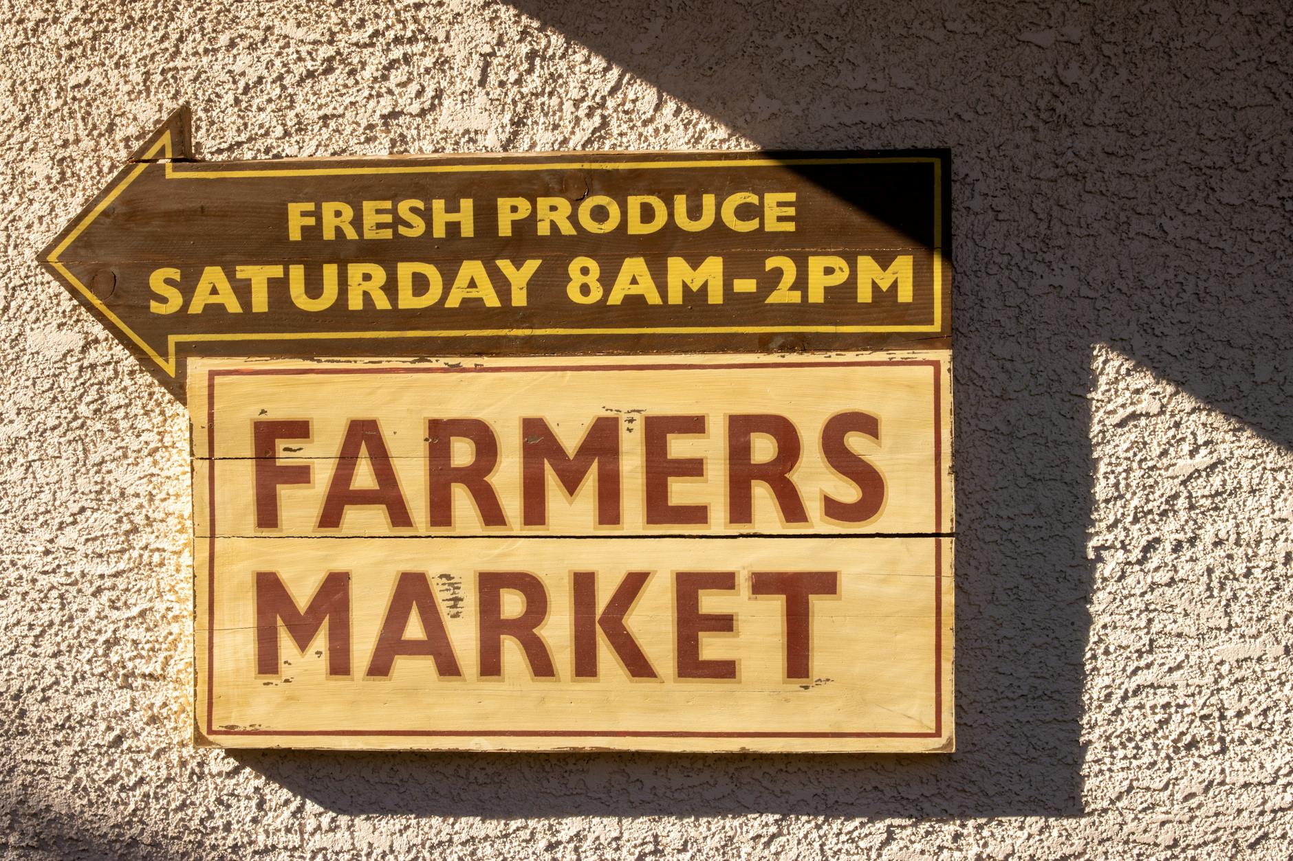 Brightly painted farmers market sign indicating fresh produce times.