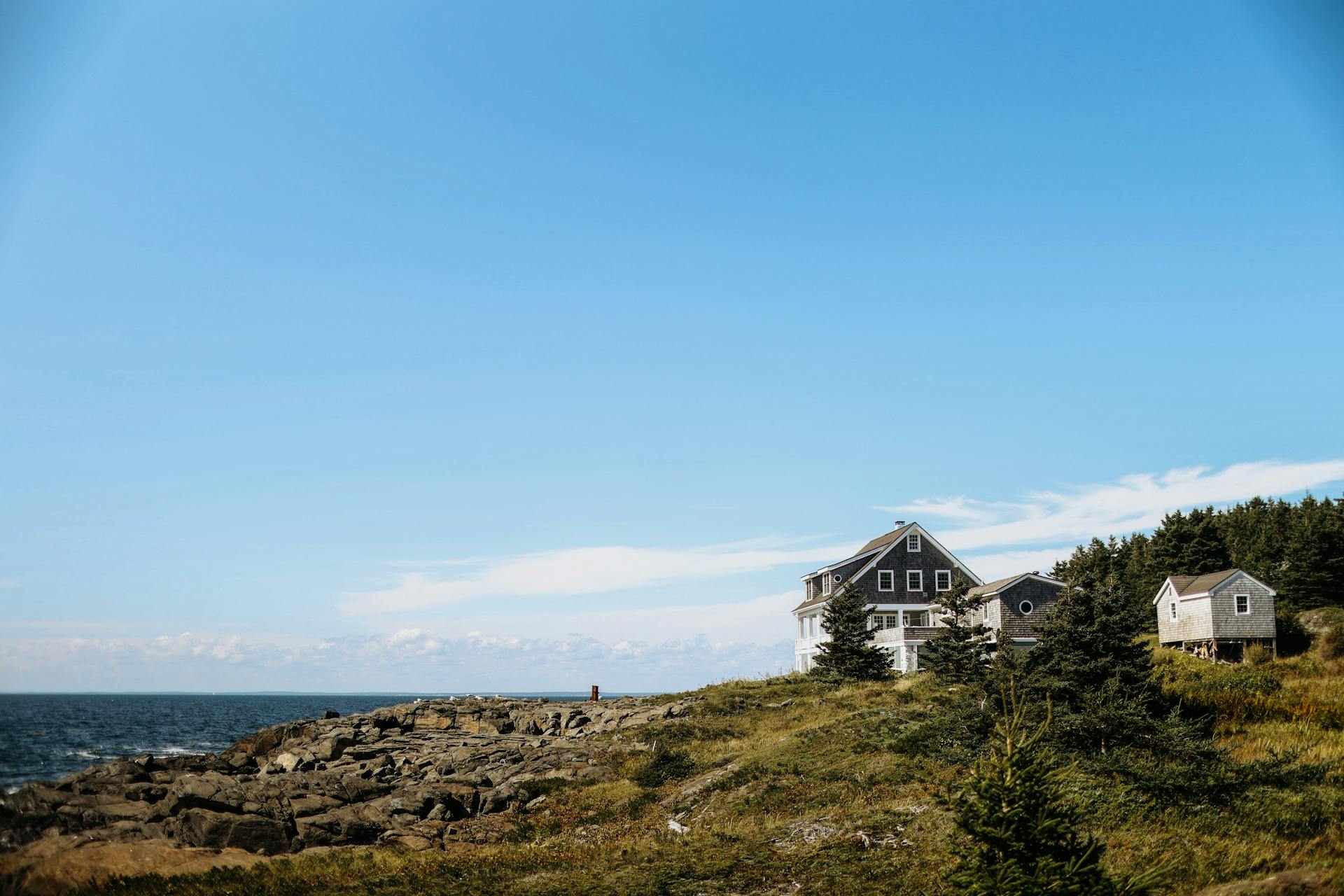 Charming houses overlooking a rocky shore on Monhegan Island with a clear blue sky backdrop.