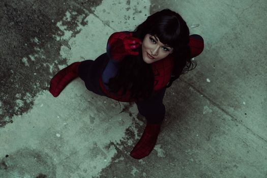 Woman in Spider-Man costume striking a dynamic pose from an overhead view on worn pavement.