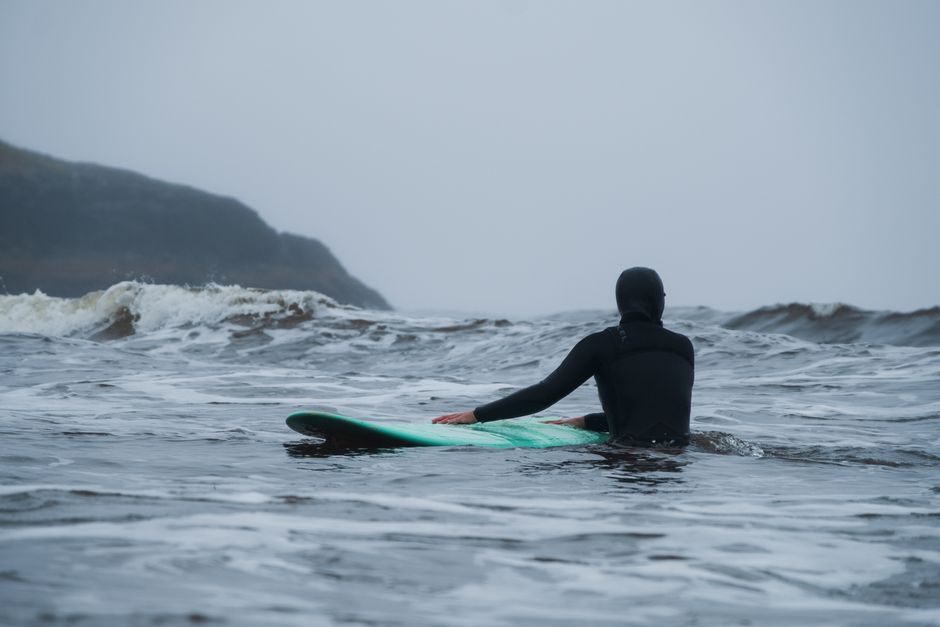 Surfer in wetsuit paddling on the ocean with overcast skies, ready to ride waves.