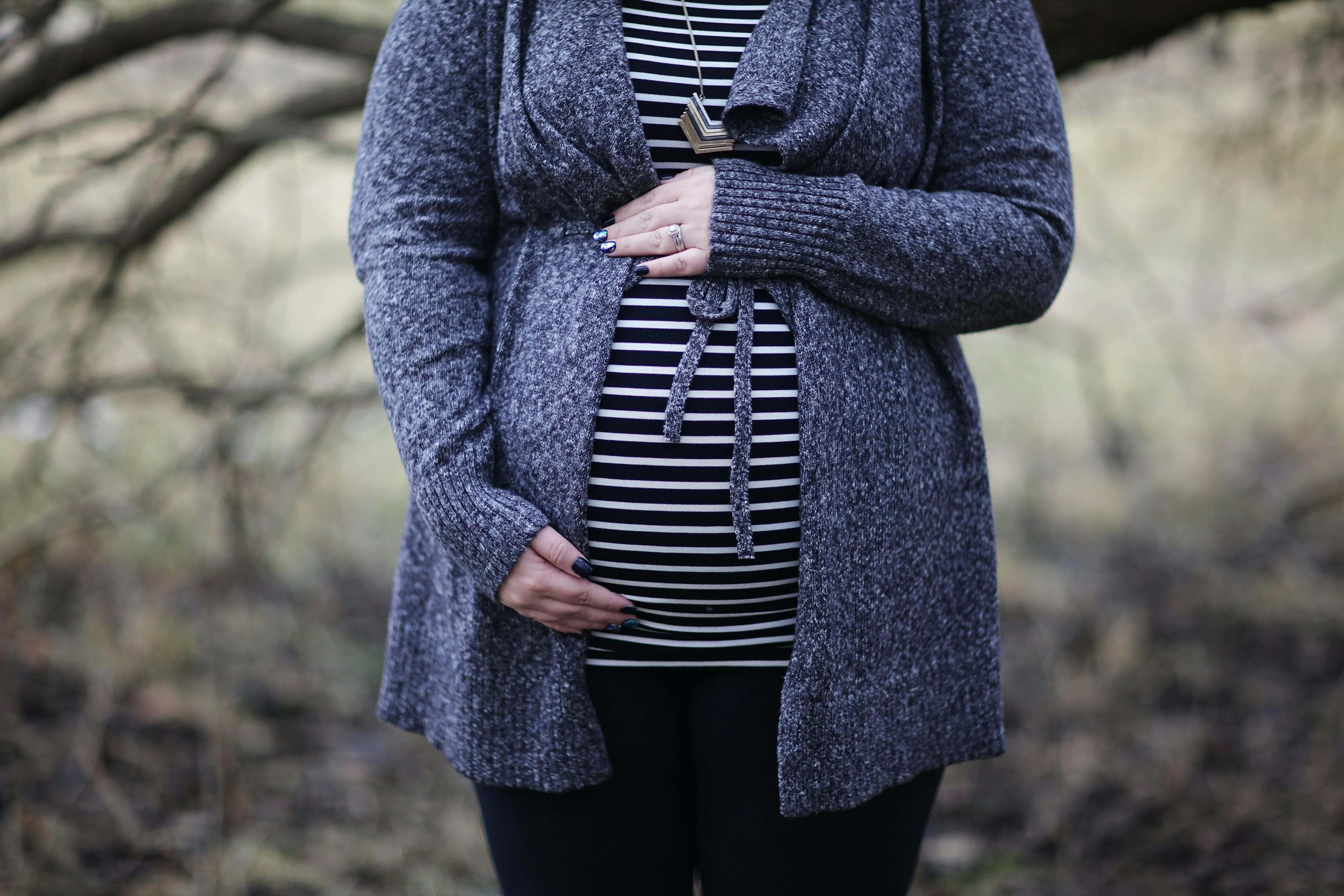 woman pregnant in black and white striped shirt standing near bare tree