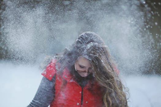 Woman enjoying snowy weather in red vest and glasses outdoors.