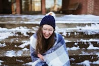 一位年轻女子戴着眼镜、无檐帽和围巾，在雪地上微笑