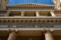Low angle view of St. Ignatius Church showing its neoclassical architecture and columns against a blue sky.