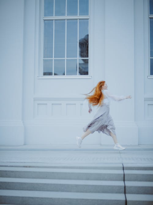 Woman in White Long Sleeve Shirt and White Pants Jumping on White Window