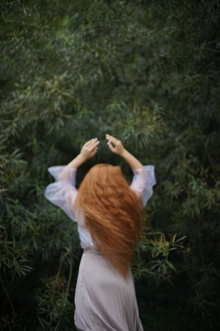Blurry image of a redhead woman twirling in a white dress amidst greenery.