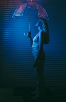 Side profile of a woman holding a clear umbrella under blue lighting indoors.