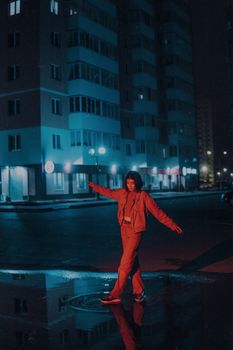 A woman joyfully dances in the rain at night in a neon-lit city street.