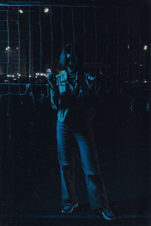 Free Dark portrait of a woman standing by a fence at night in an urban setting. Atmospheric and mysterious. Stock Photo