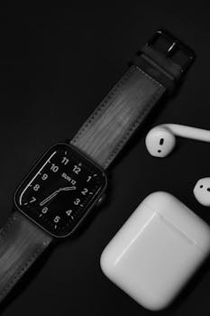 Stylish black and white flatlay featuring a wristwatch and wireless earphones on a dark background.